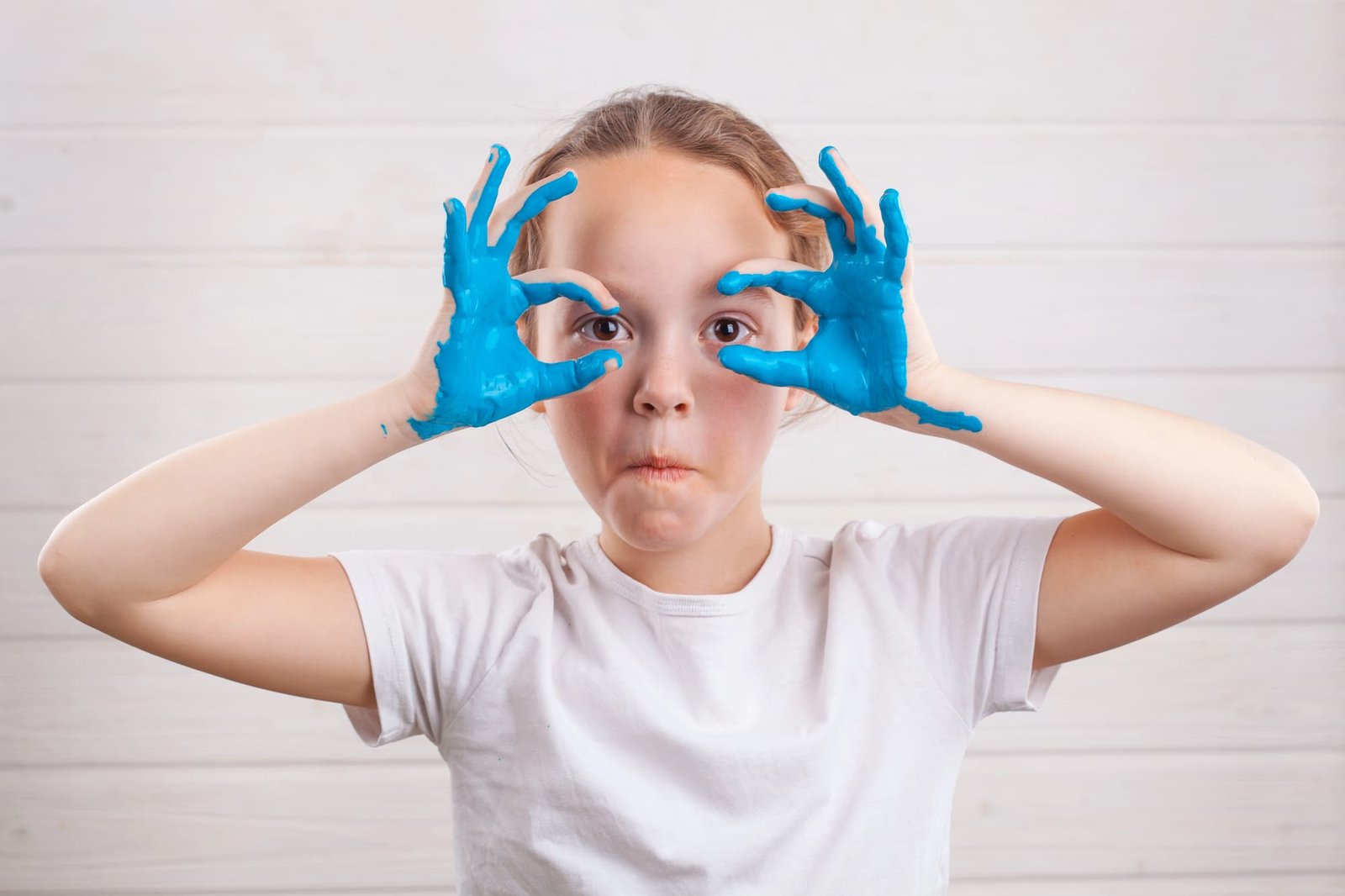 Girl making silly face with blue paint on her hands