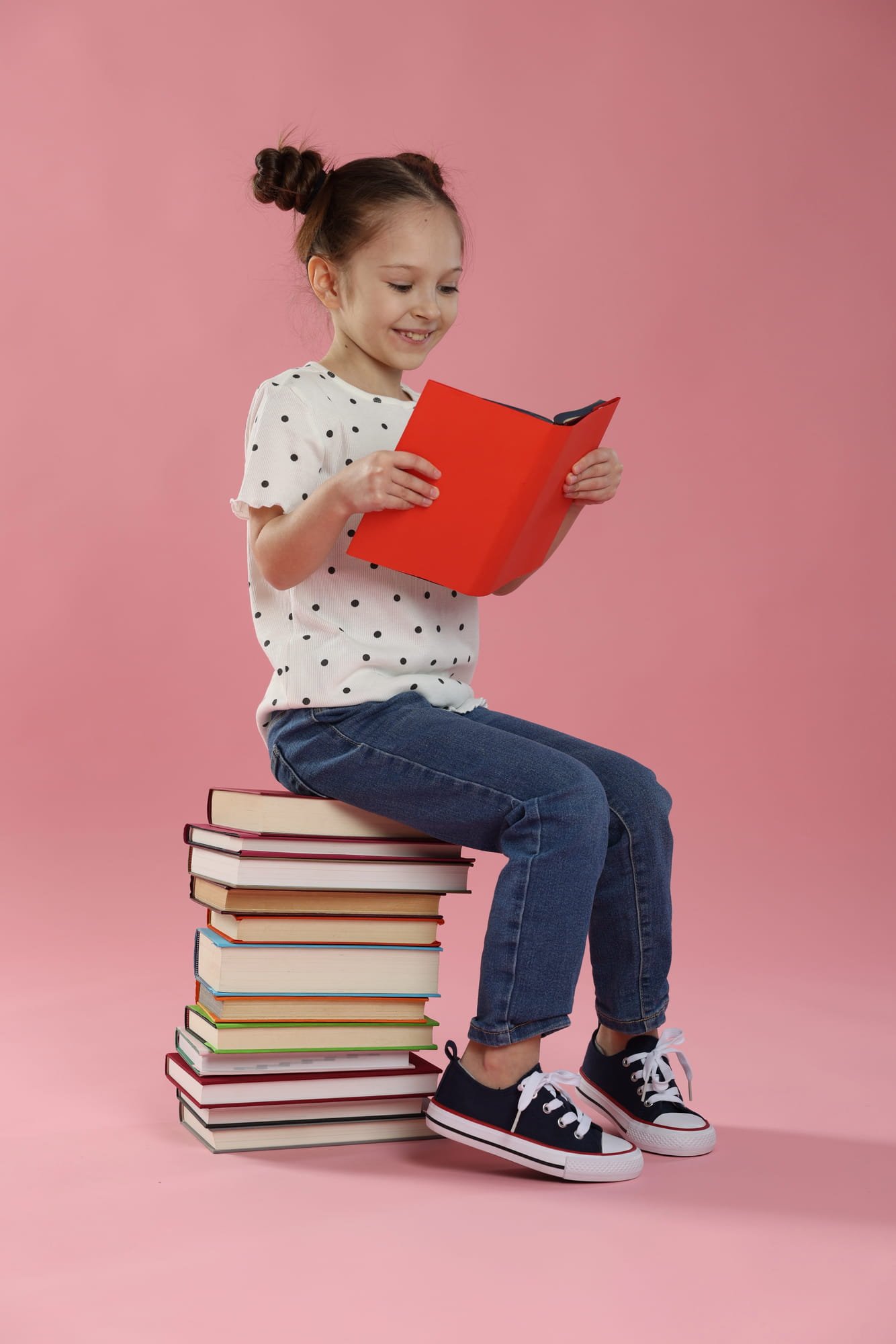 Girl reading a book while sitting on a stack of books